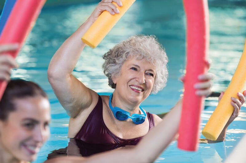 Senior woman exercising with pool noodles