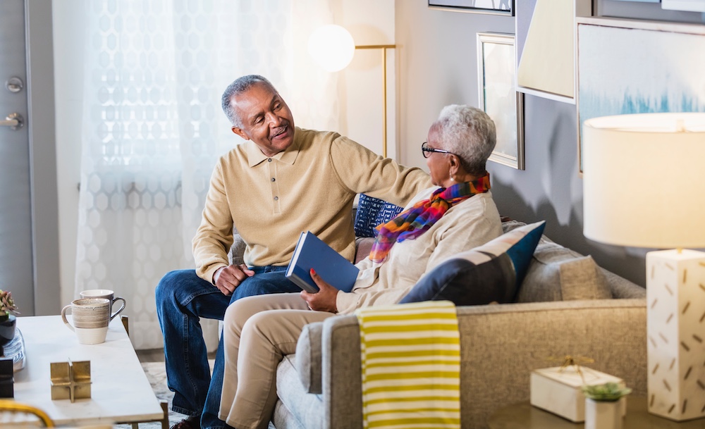 senior couple sitting on couch surrounded by packing boxes